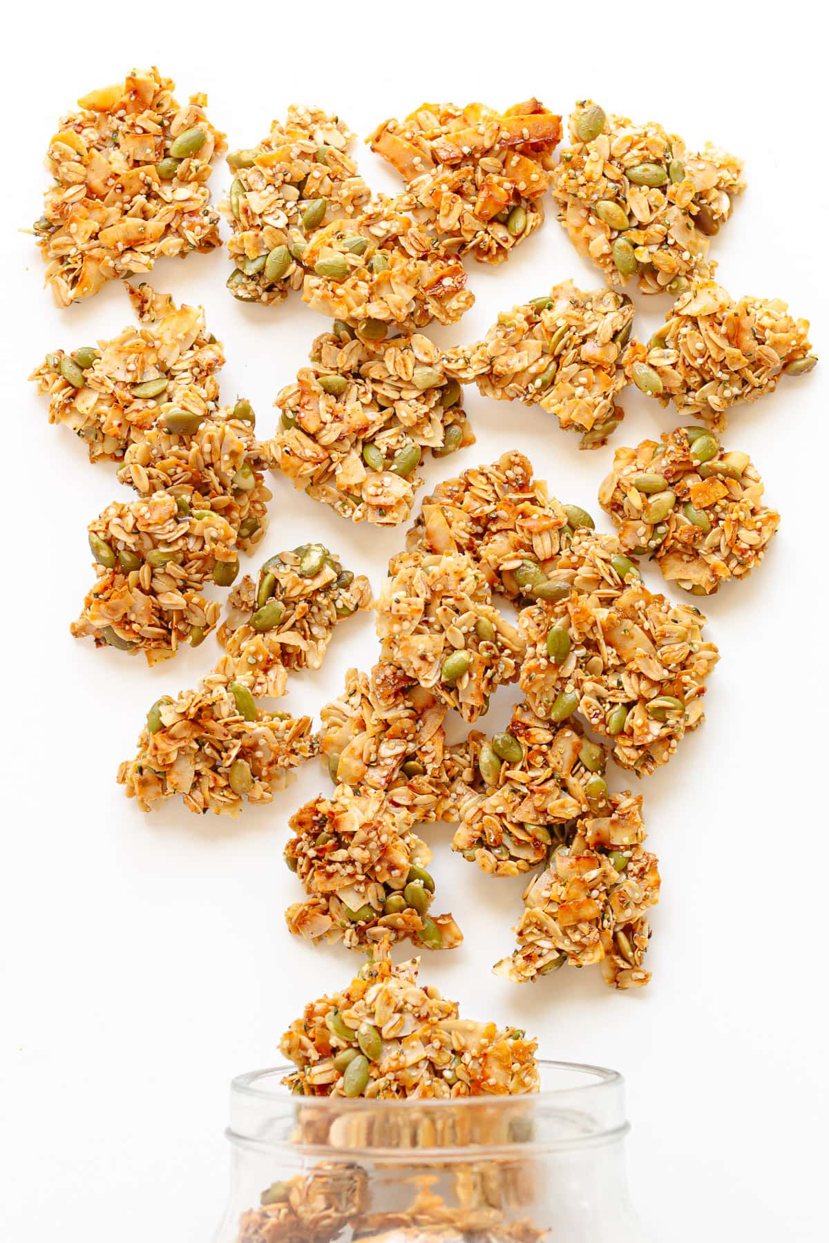 Granola clusters pouring out of a jar onto a white surface.