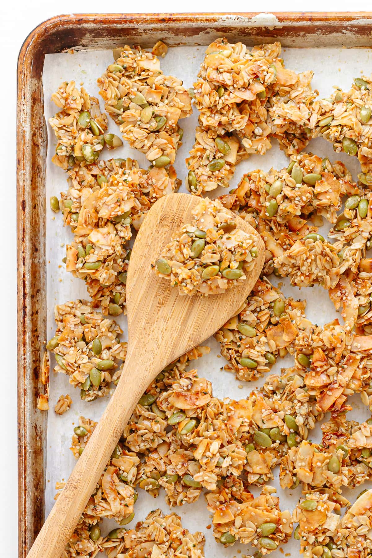 Granola clusters on baking sheet with wooden spoon.