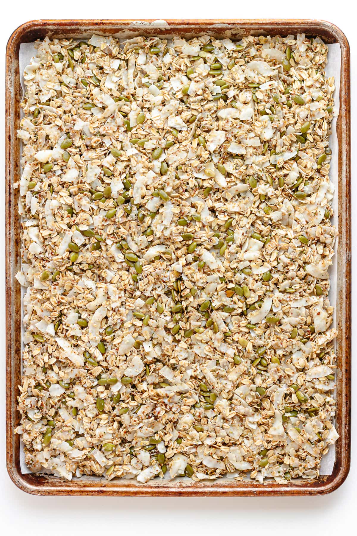 Uncooked coconut granola spread out evenly on a large baking sheet.