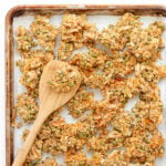 Vanilla coconut granola clusters on a baking sheet with wooden spatula.