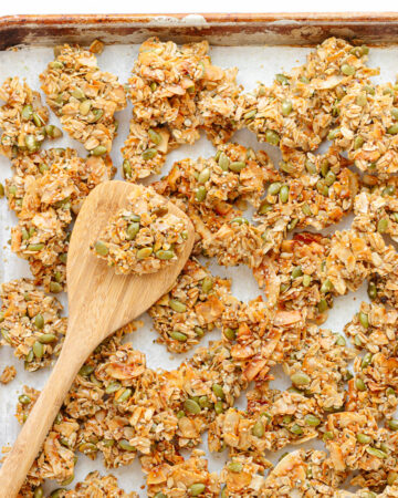 Vanilla coconut granola clusters on a baking sheet with wooden spatula.