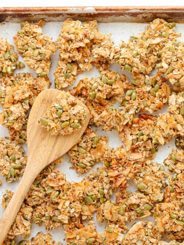 Vanilla coconut granola clusters on a baking sheet with wooden spatula.