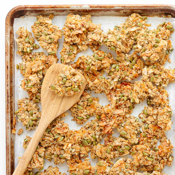 Vanilla coconut granola clusters on a baking sheet with wooden spatula.