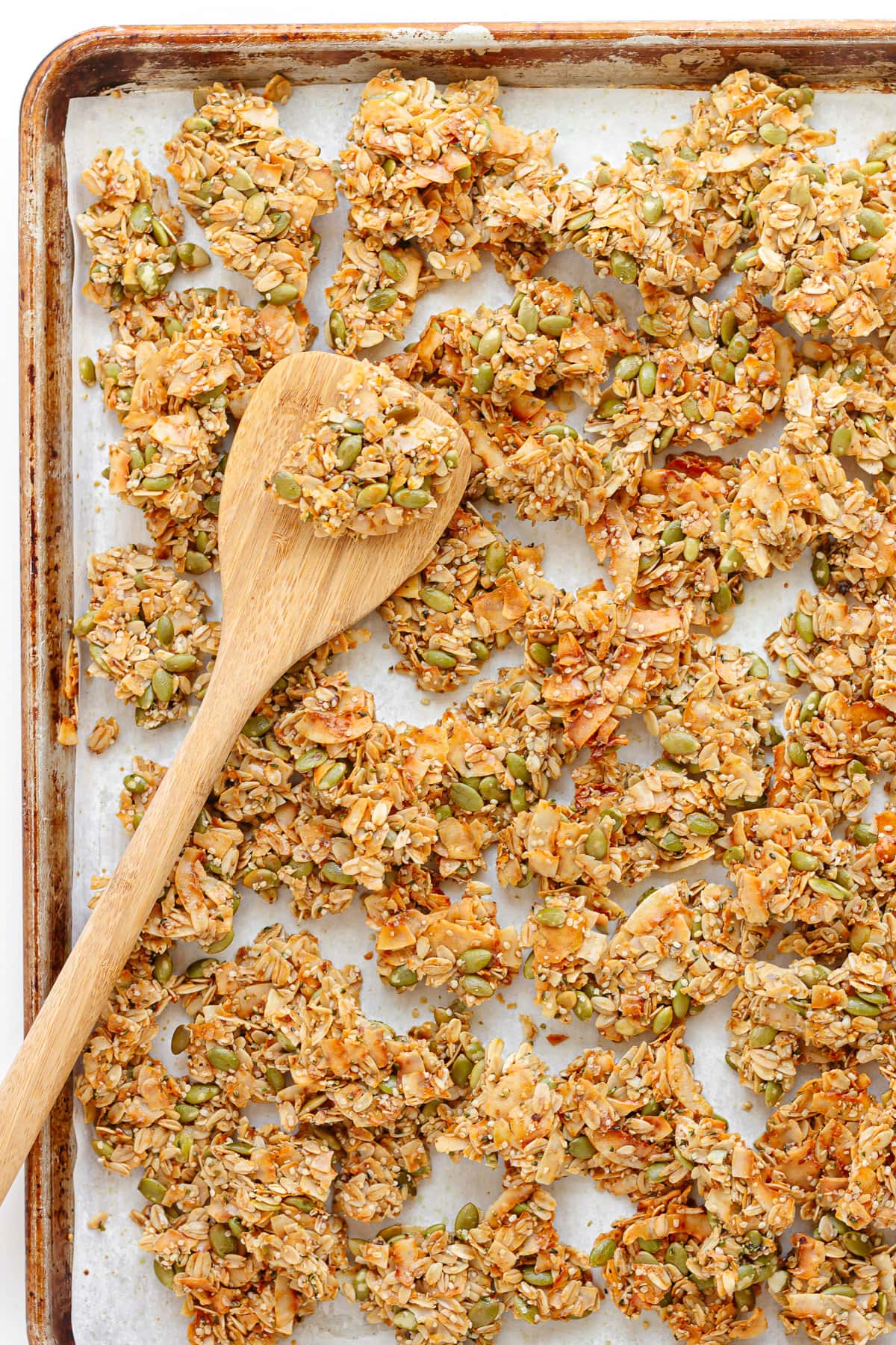 Vanilla coconut granola clusters on a parchment paper lined baking sheet with a wooden spatula.
