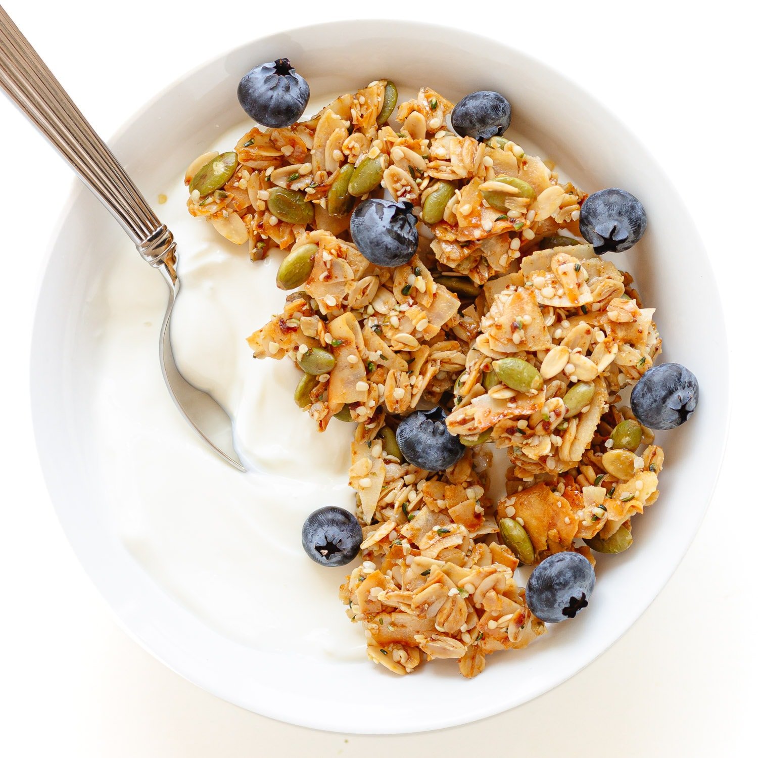 Yogurt topped with vanilla coconut granola and blueberries in a white bowl with spoon.