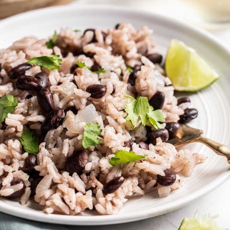 Black beans and rice on a white plate garnished with cilantro and a lime wedge.