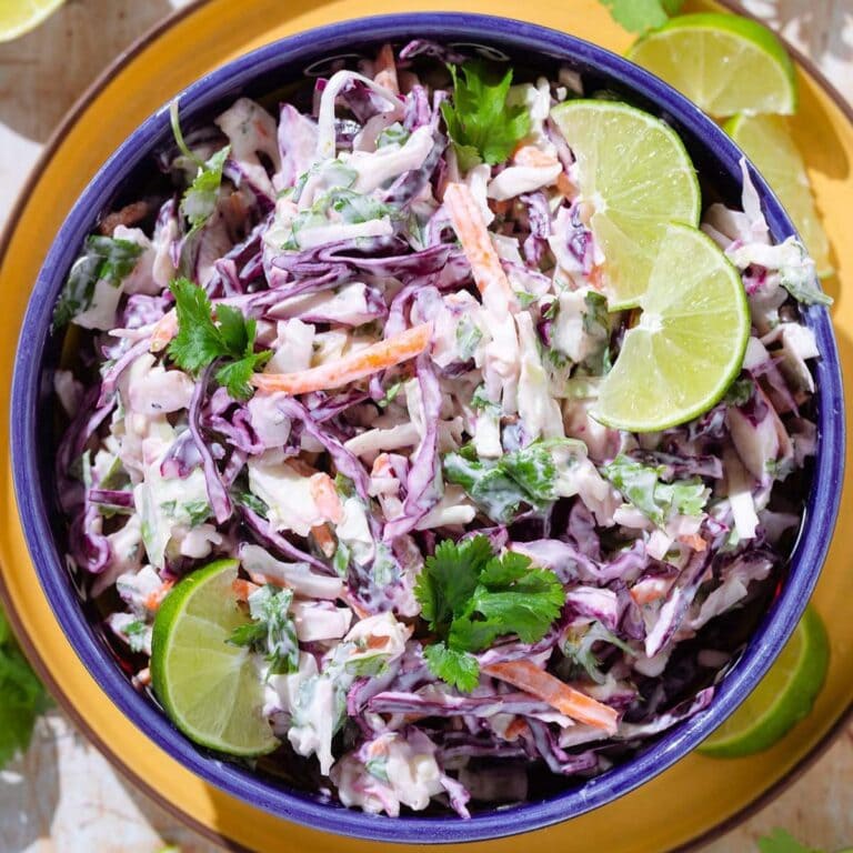 Cilantro Lime Slaw in a blue serving bowl garnished with lime slices and cilantro.