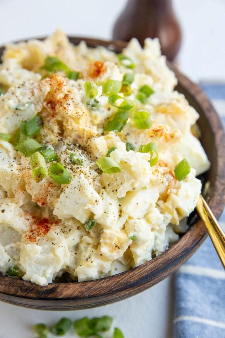 Potato salad garnished with green onions in a wooden serving bowl.