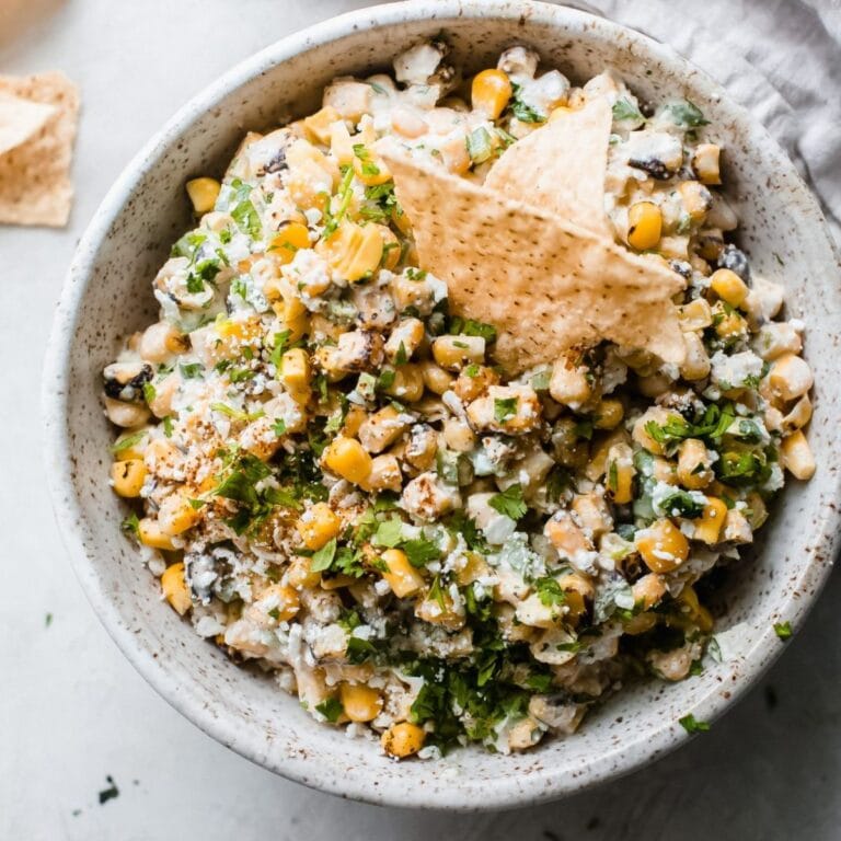 Mexican street corn dip in a grey bowl with tortilla chips dipped in.
