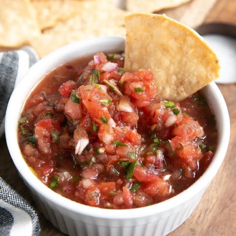 Salsa in a white ramekin with a tortilla chip dipped in.