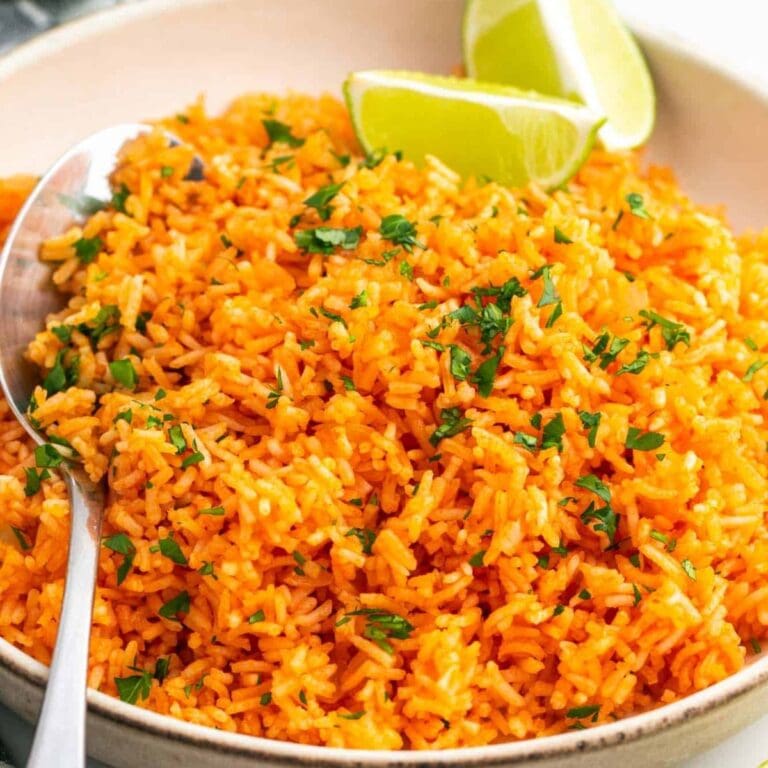 Mexican rice in a serving bowl garnished with chopped cilantro and lime wedges.