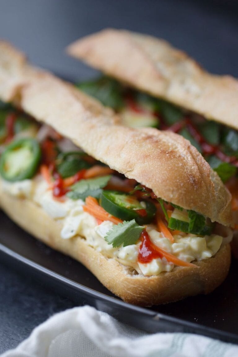 Two egg salad banh mi sandwiches on a black plate with white linen napkin.