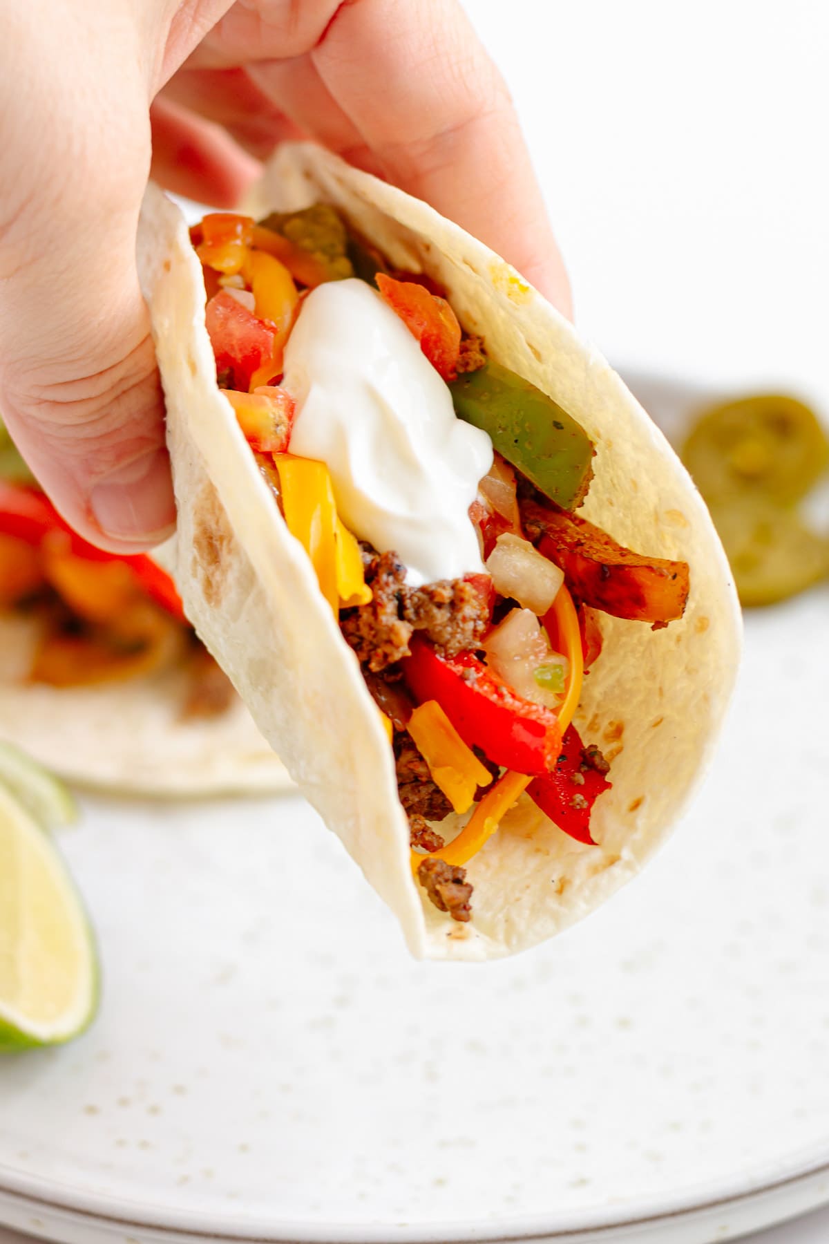 Hand holding a ground beef fajita on a flour tortilla.