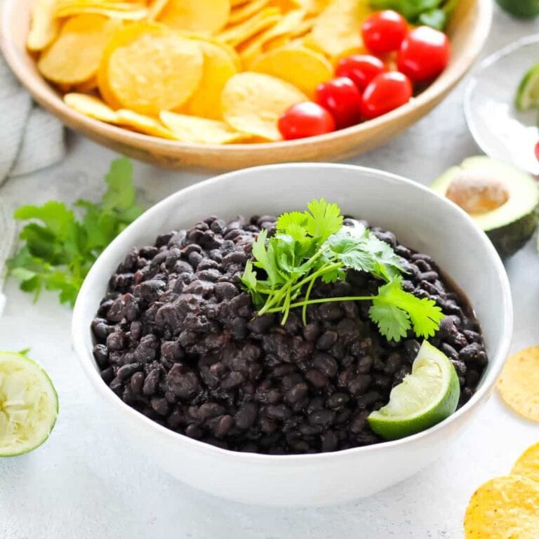 White bowl of black beans garnished with cilantro and a lime wedge.