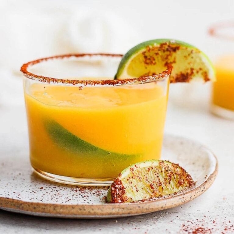 Mango margarita garnished with tajin and lime wedges.