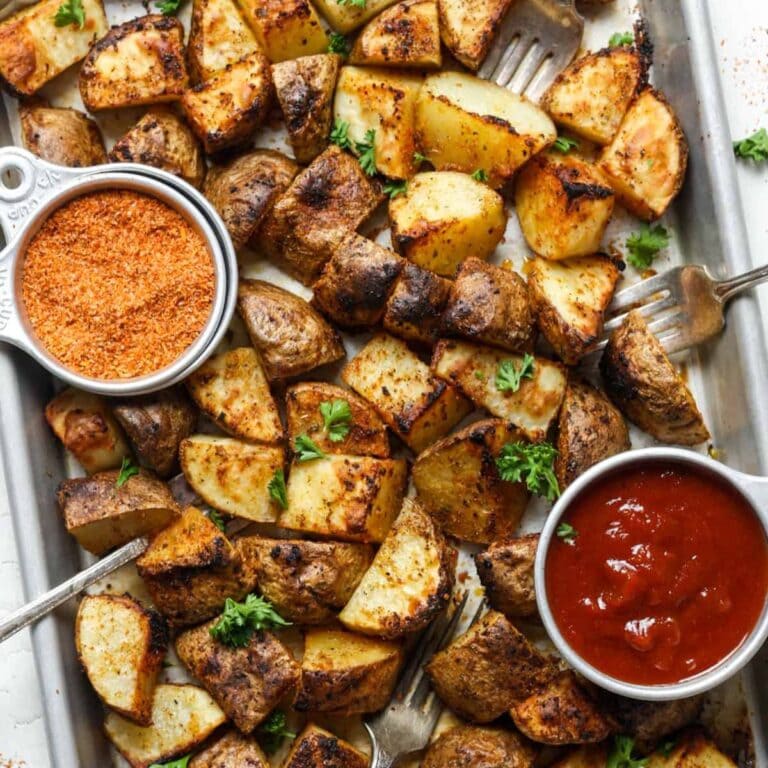 Mexican potatoes on a sheet pan with bowls of ketchup and seasoning salt.