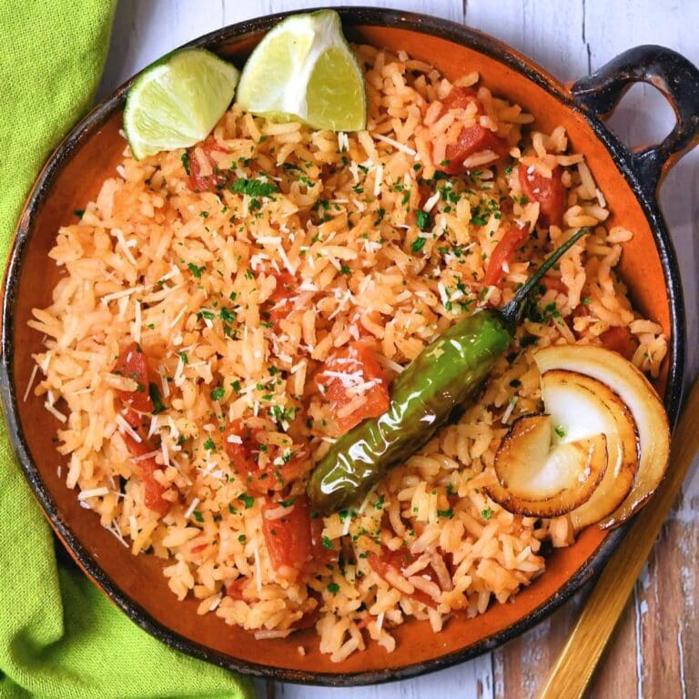 Mexican red rice in a pan garnished with lime wedges, chili, onion and cilantro.