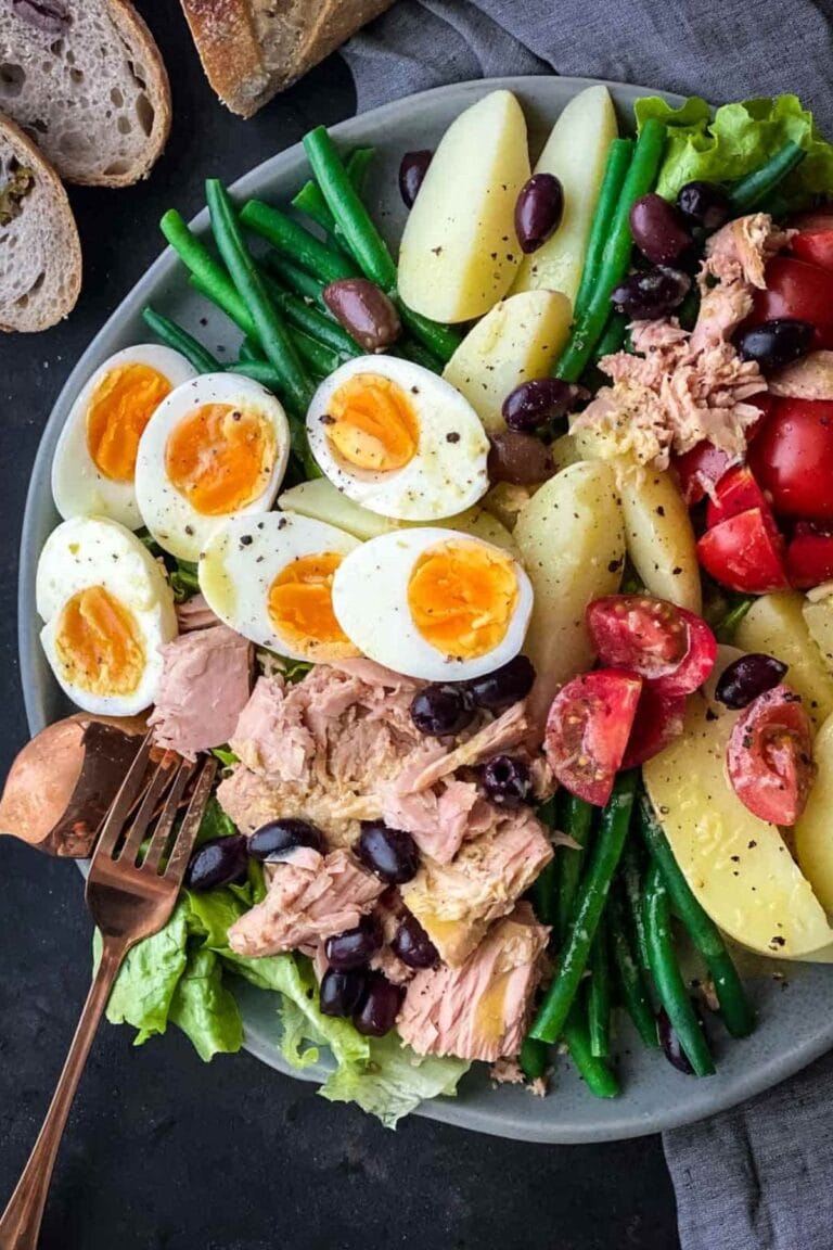 Salad Nicoise on a blue plate with a grey linen and gold colored fork and spoon.