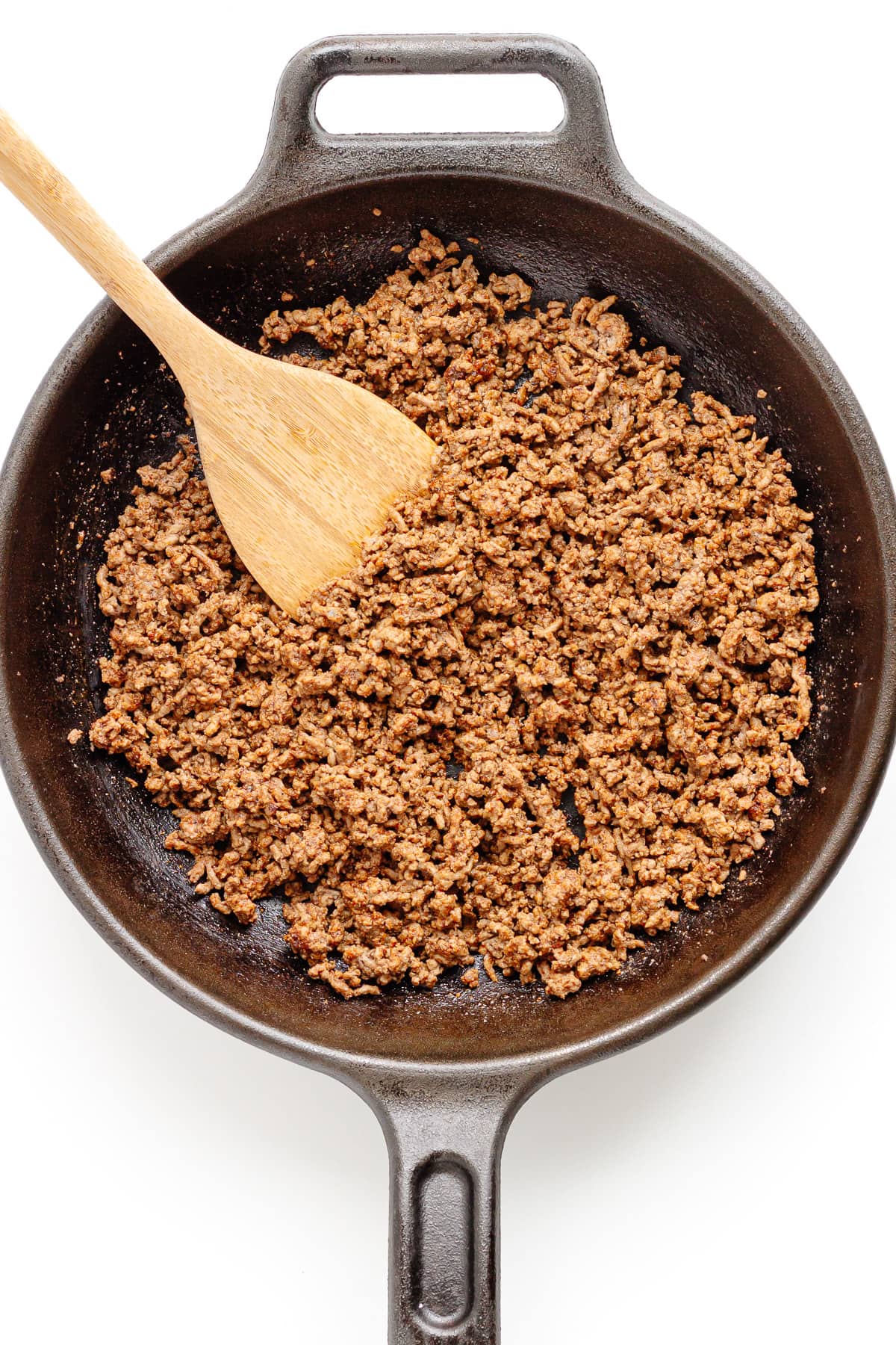 Browned ground beef seasoned with fajita seasoning in a cast iron skillet with wooden spoon.