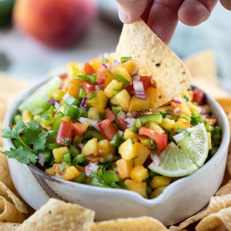 Hand dipping a tortilla chip into a bowl of spicy peach salsa.