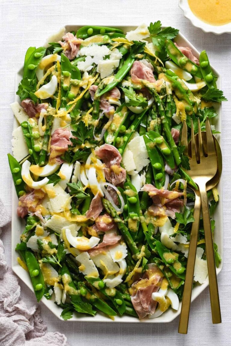 A spring salad that is loaded with seasonal ingredients including asparagus, snap peas, prosciutto and cheese and topped with a deviled egg dressing,