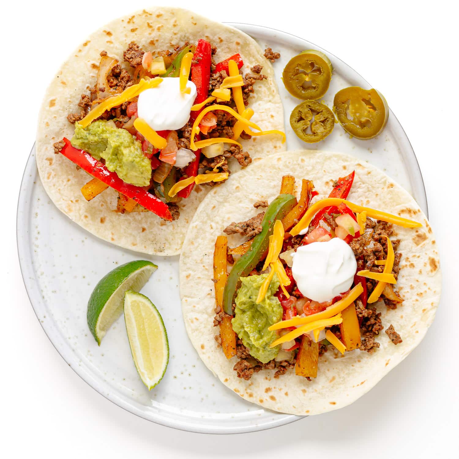 Two open ground beef fajitas on a plate with lime wedges and pickled jalapeno slices next to it.