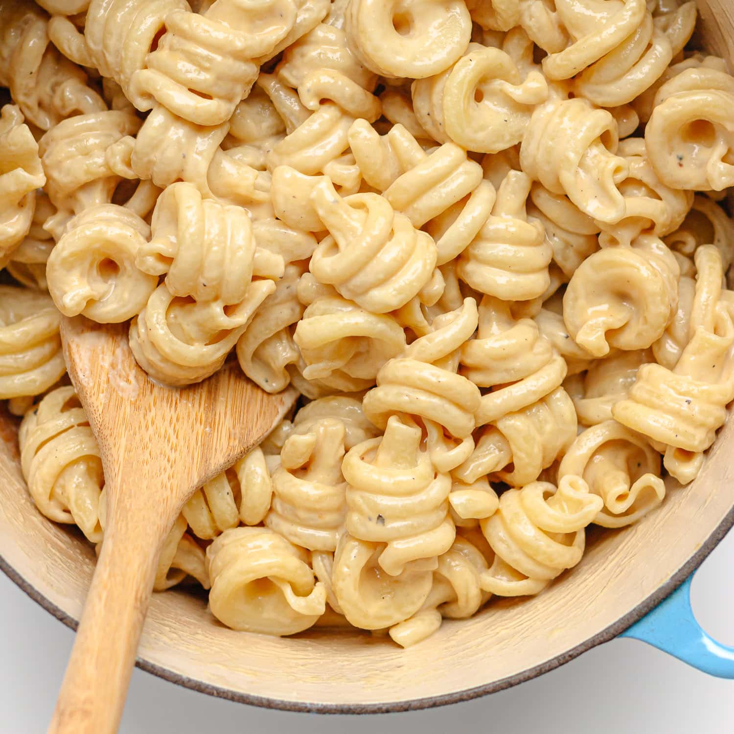 Pasta being mixed with tahini sauce in a pot with a wooden spoon.