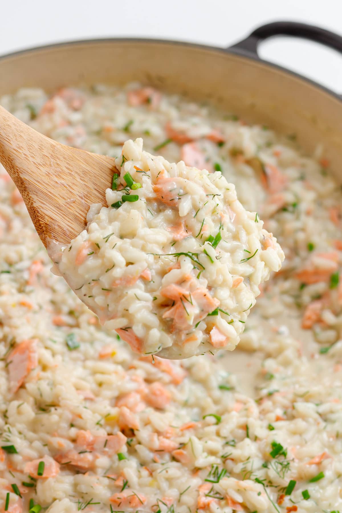 Wooden spoon lifting up salmon risotto from pan.