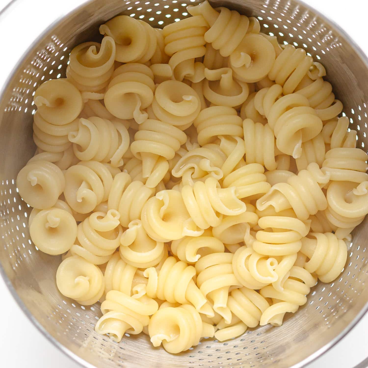 Drained cooked pasta in a stainless steel strainer.