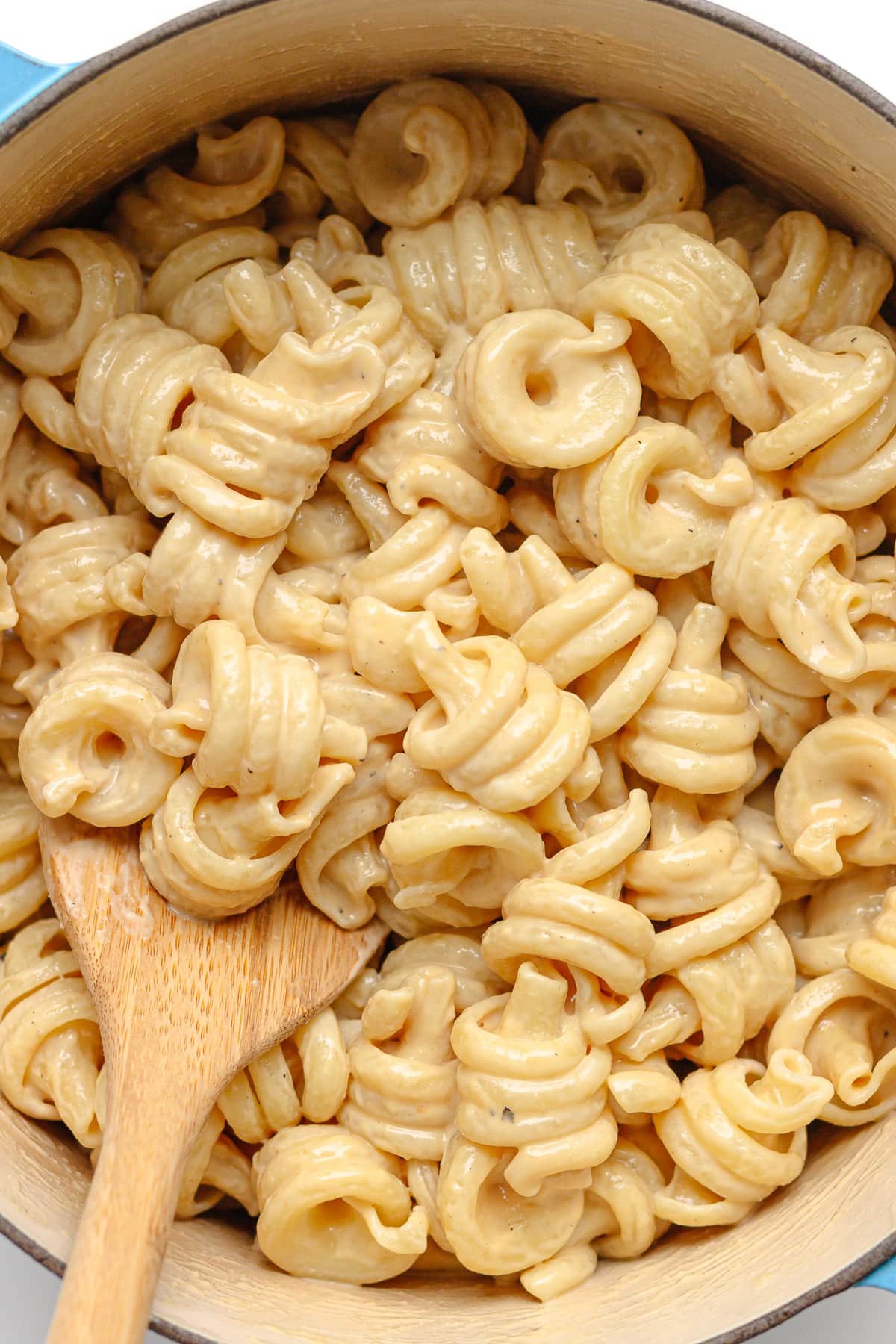 Pasta with creamy tahini sauce in a dutch oven with wooden spoon.