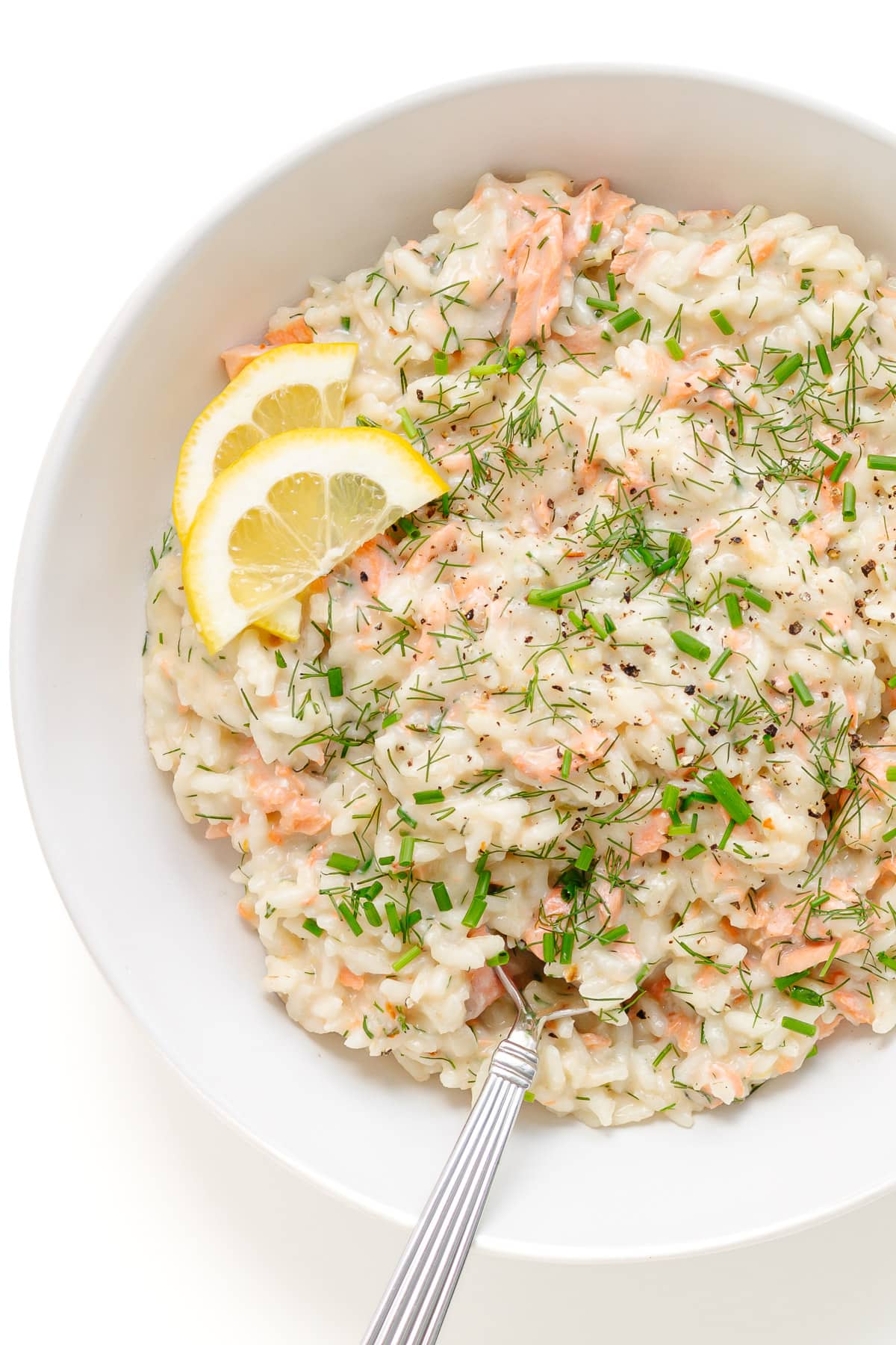 Risotto with salmon and lemon served in a white bowl with spoon.