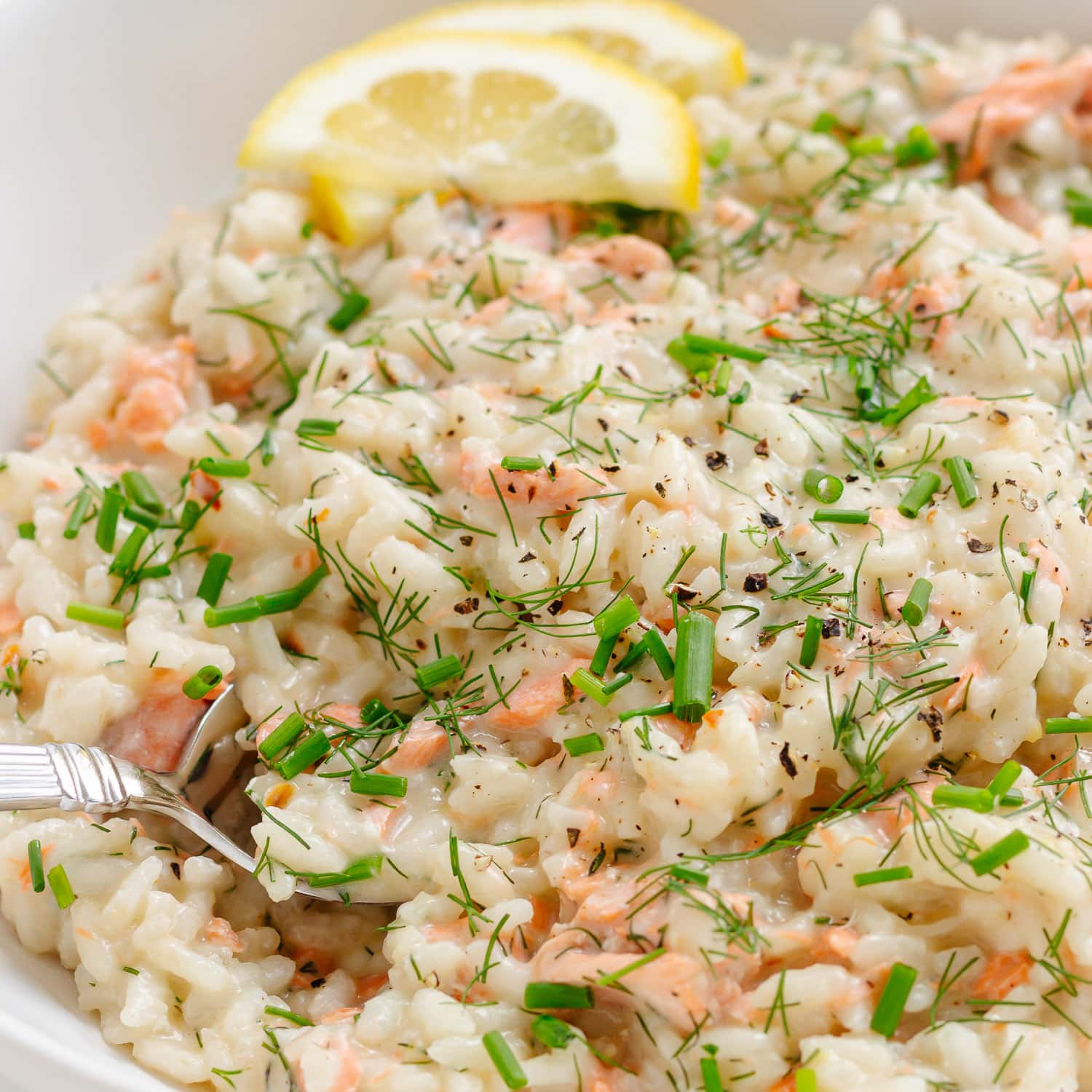 Salmon risotto garnished with lemon slices and chopped fresh dill and chives.