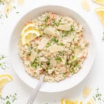 White bowl of salmon risotto garnished with lemon slices, shaved parmesan, fresh dill and chives.