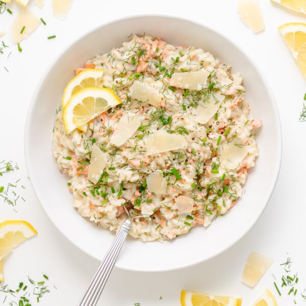 White bowl of salmon risotto garnished with lemon slices, shaved parmesan, fresh dill and chives.