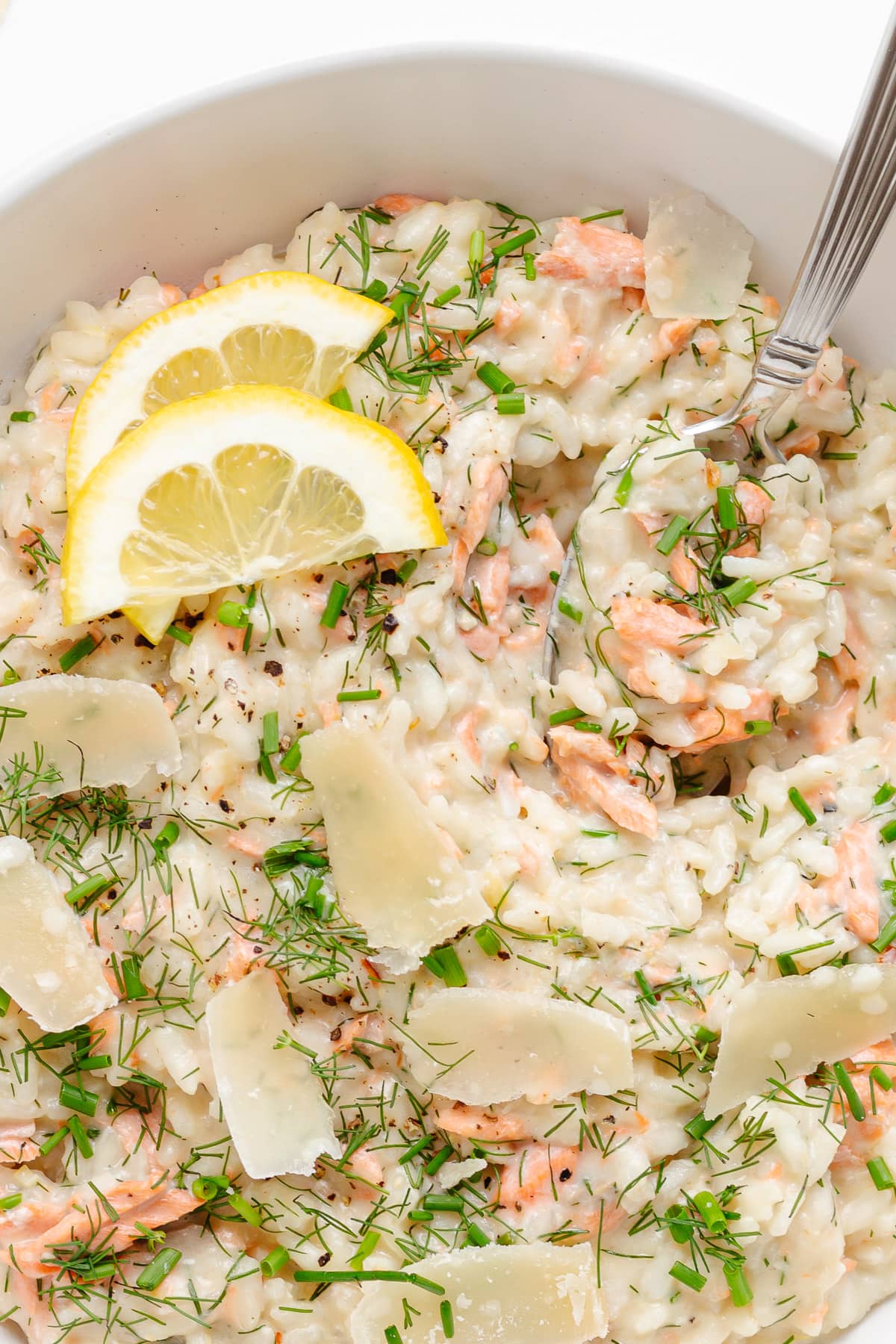 Closeup of salmon risotto served in a white bowl with spoon.