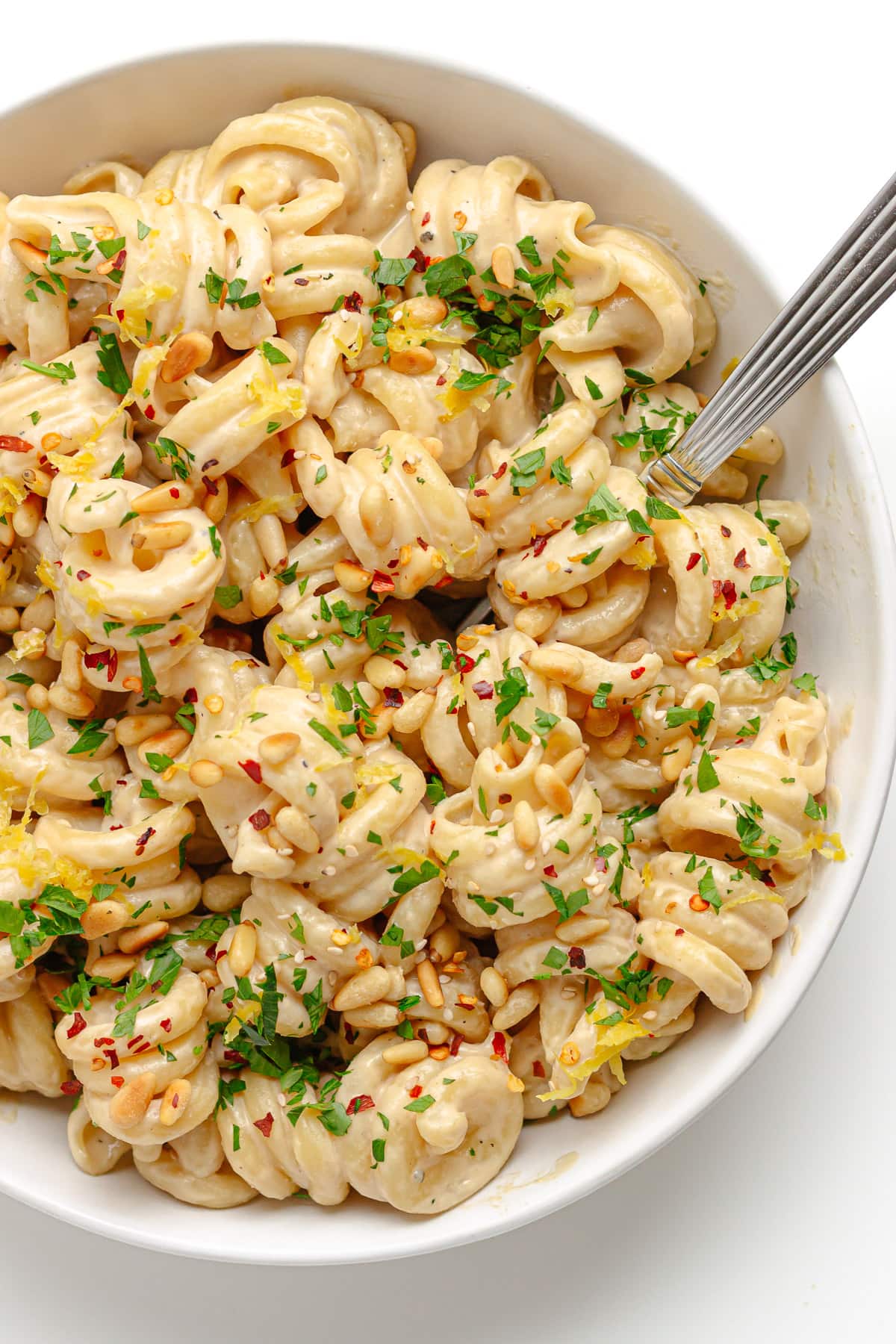 White bowl of tahini pasta with fork.