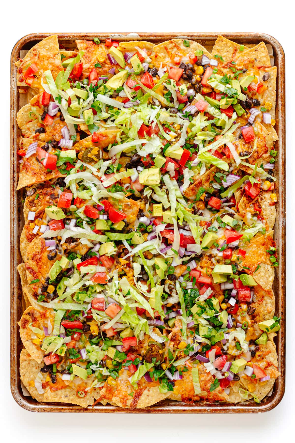 Fully loaded vegetarian sheet pan nachos on a white background.