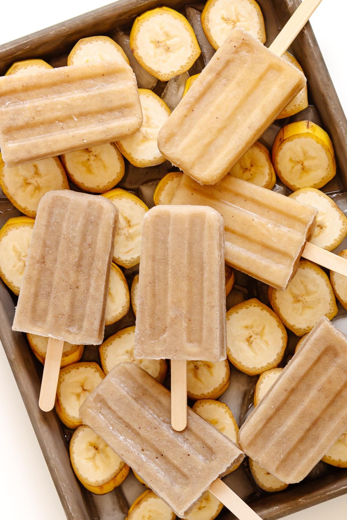 Banana popsicles sitting on a tray of banana slices.