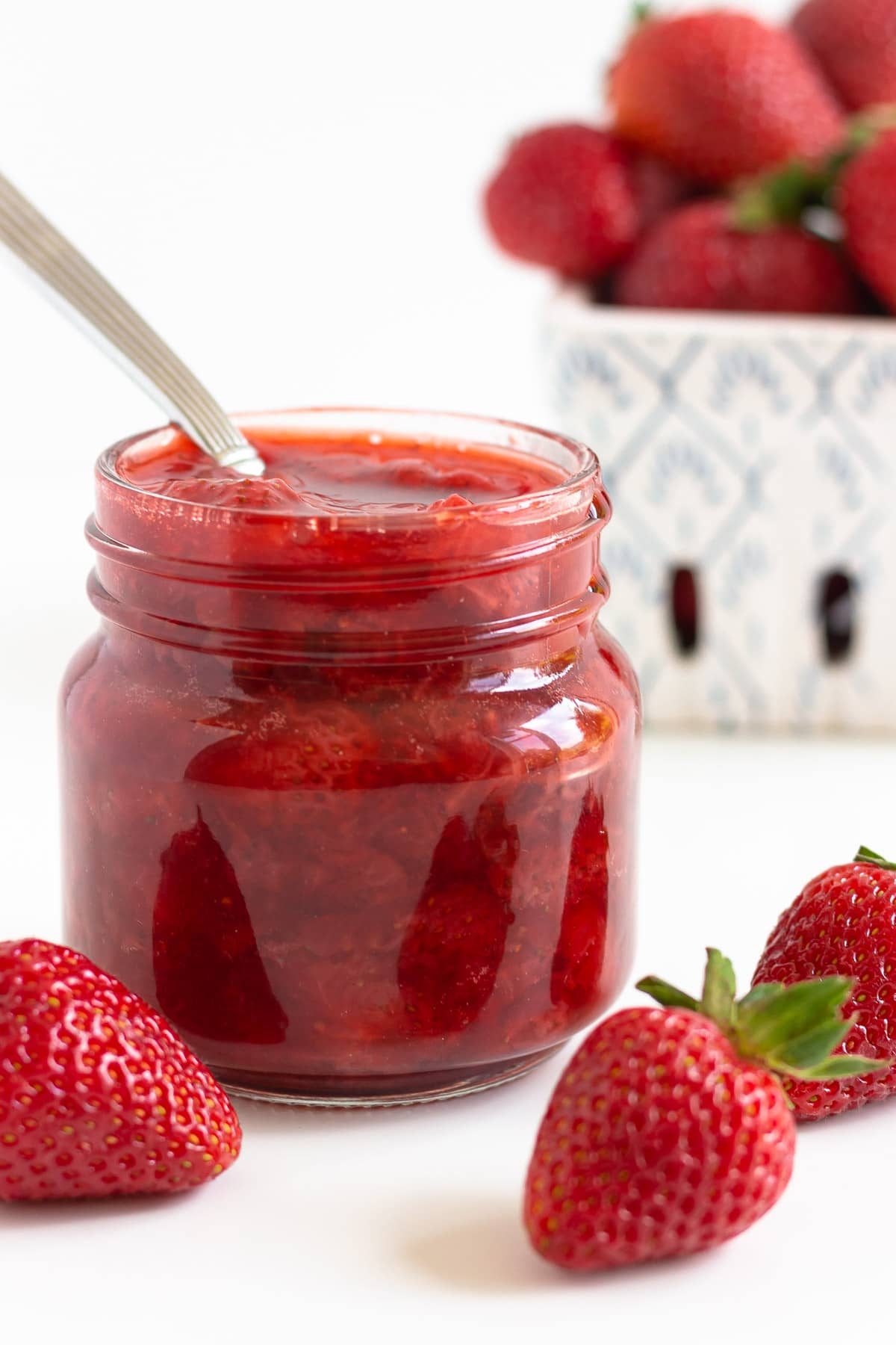 Jar of strawberry compote with fresh strawberries around it.