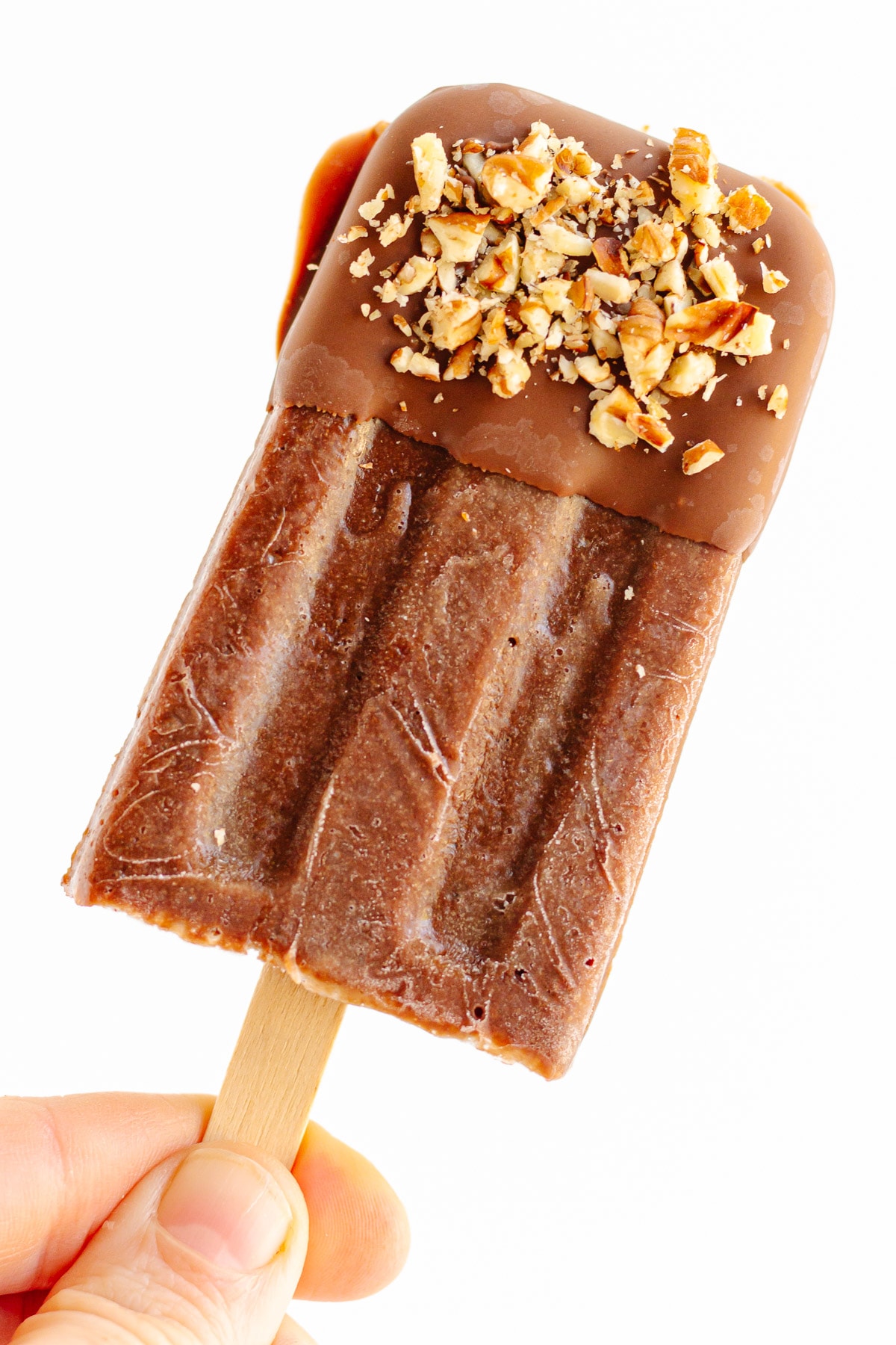 Hand holding a chocolate banana popsicle that is dipped in chocolate and chopped nuts.