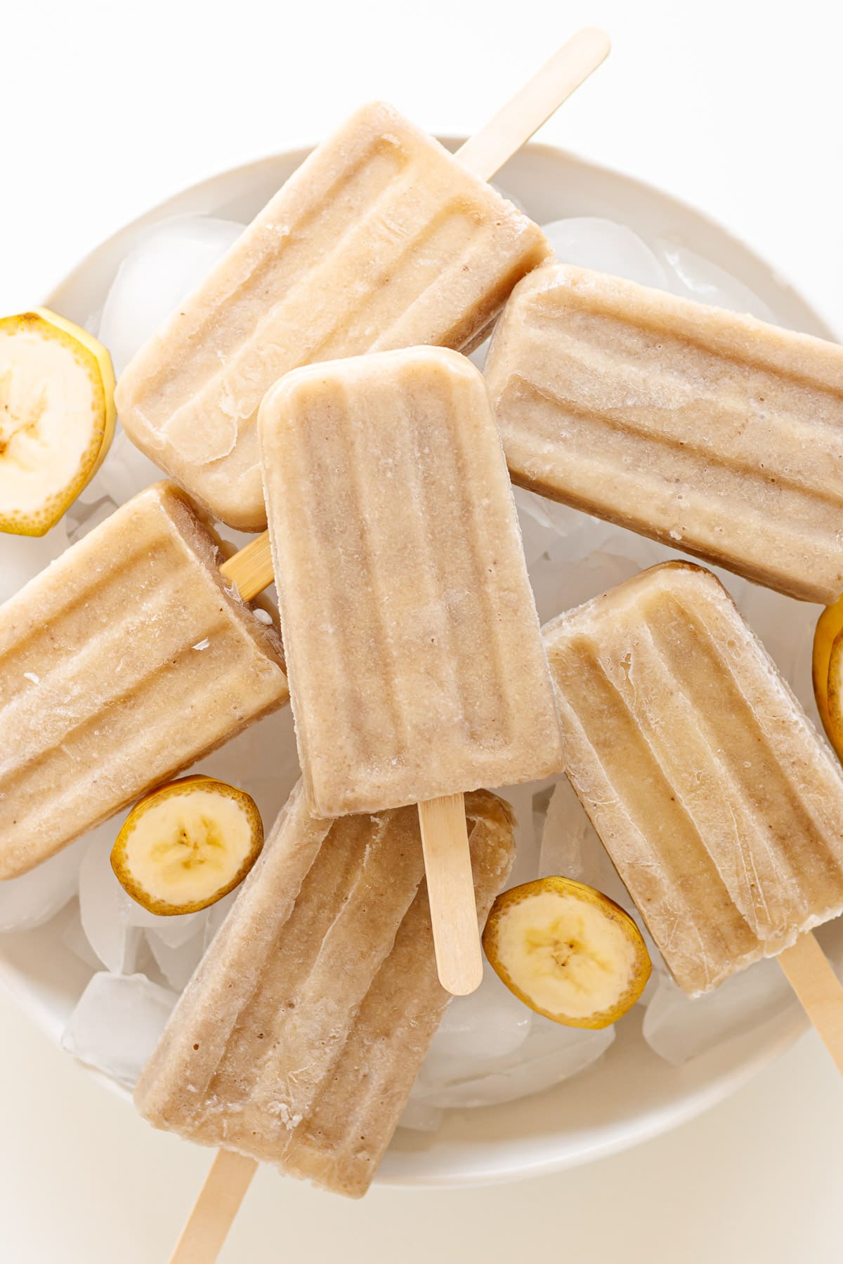 Banana popsicles piled on top of a large white serving bowl of ice.
