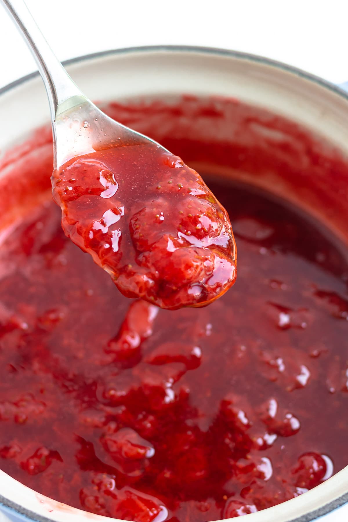 Spoon lifting homemade strawberry compote out of saucepan.