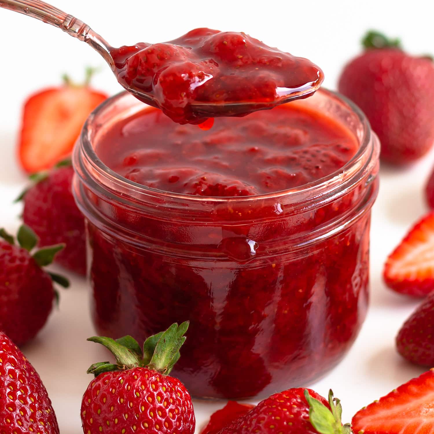 Homemade strawberry sauce in a jar with spoon scooping some out.