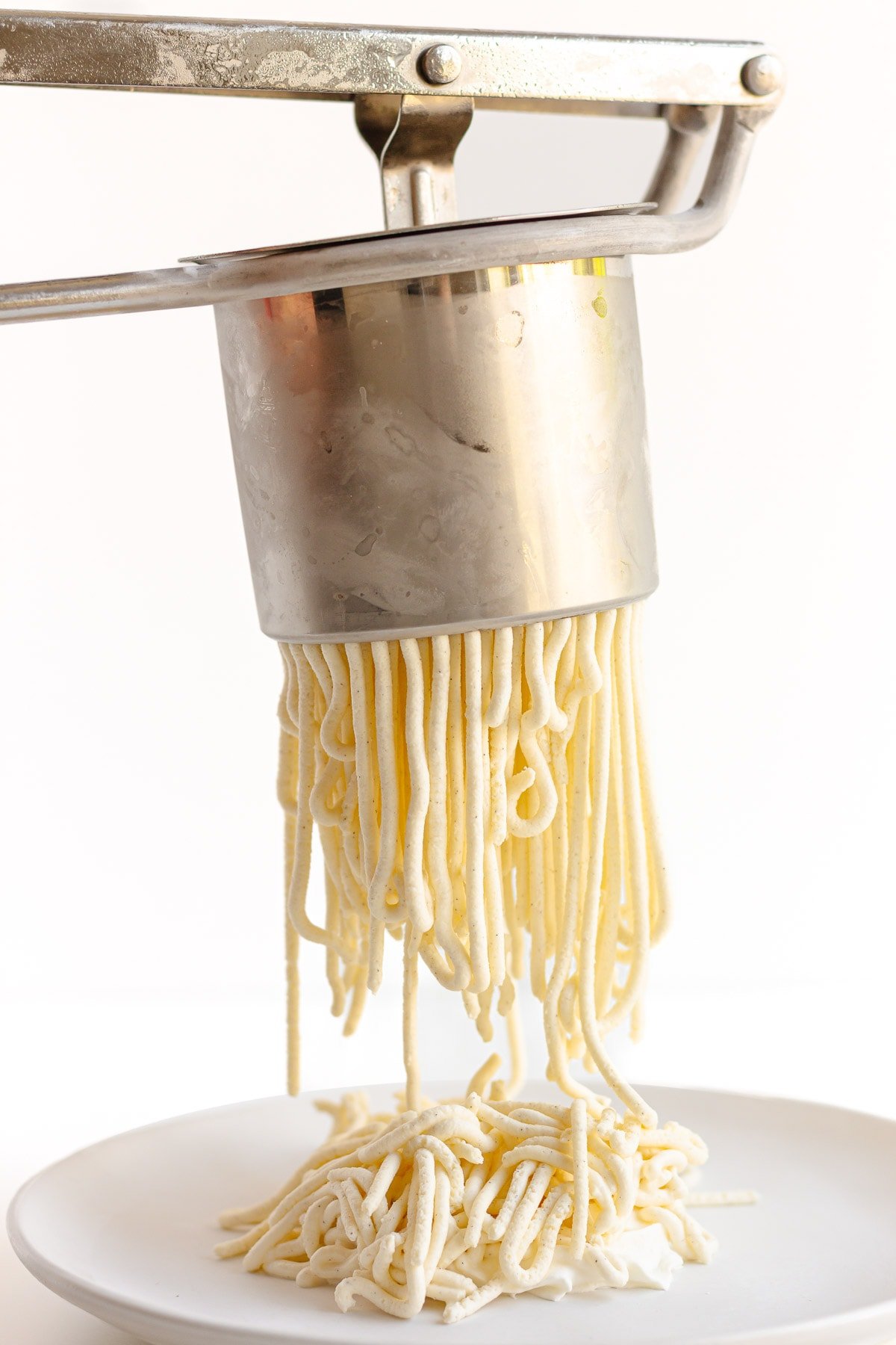 Vanilla ice cream being pressed through a potato ricer to form ice cream "spaghetti" noodles.
