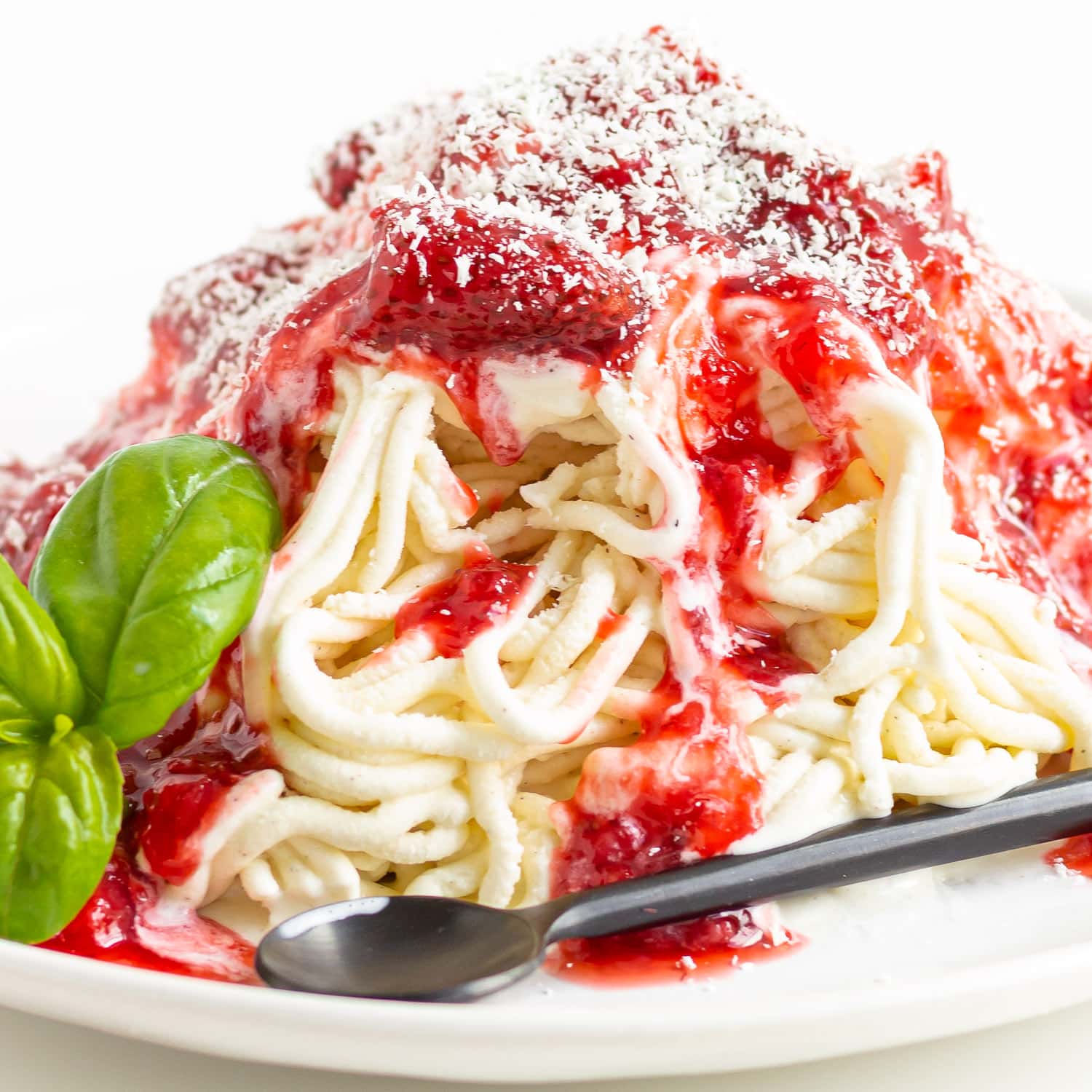 Spaghetti Eis dessert on a white plate with a sprig of basil and a black spoon.