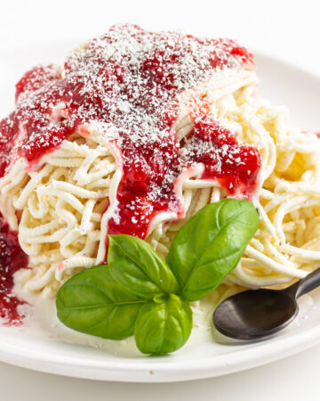 Spaghetti-Eis on a white plate with sprig of basil and a black spoon.