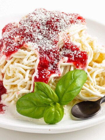 Spaghetti-Eis on a white plate with sprig of basil and a black spoon.