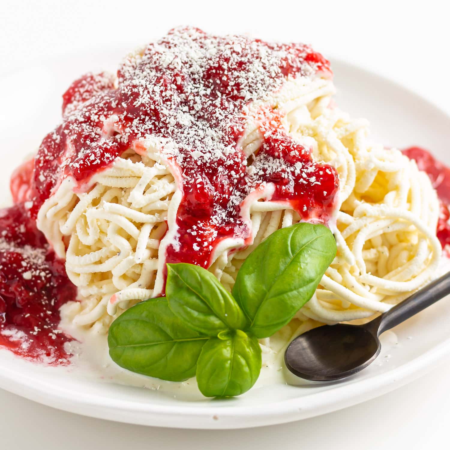 Spaghetti-Eis on a white plate with sprig of basil and black spoon.