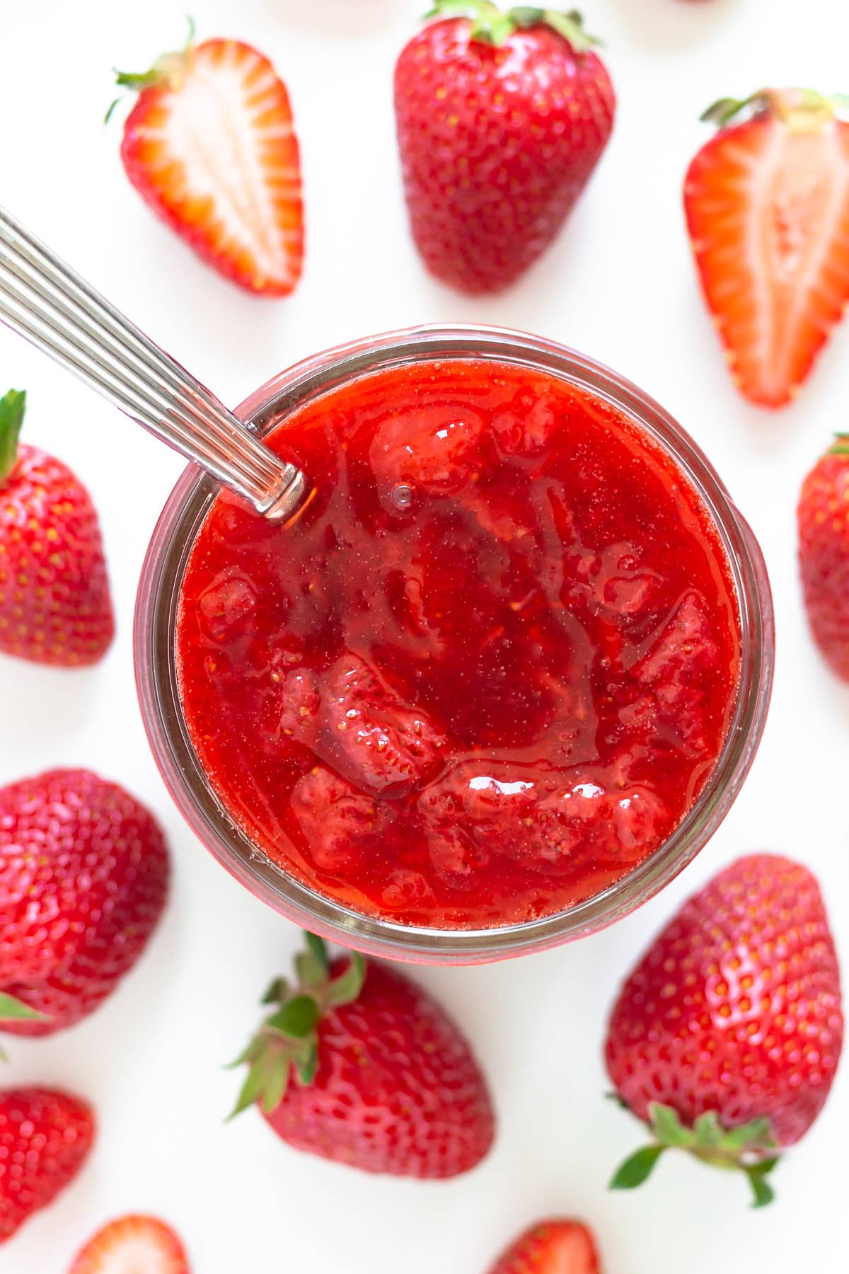 Overhead of strawberry sauce in a jar surround by fresh strawberries.