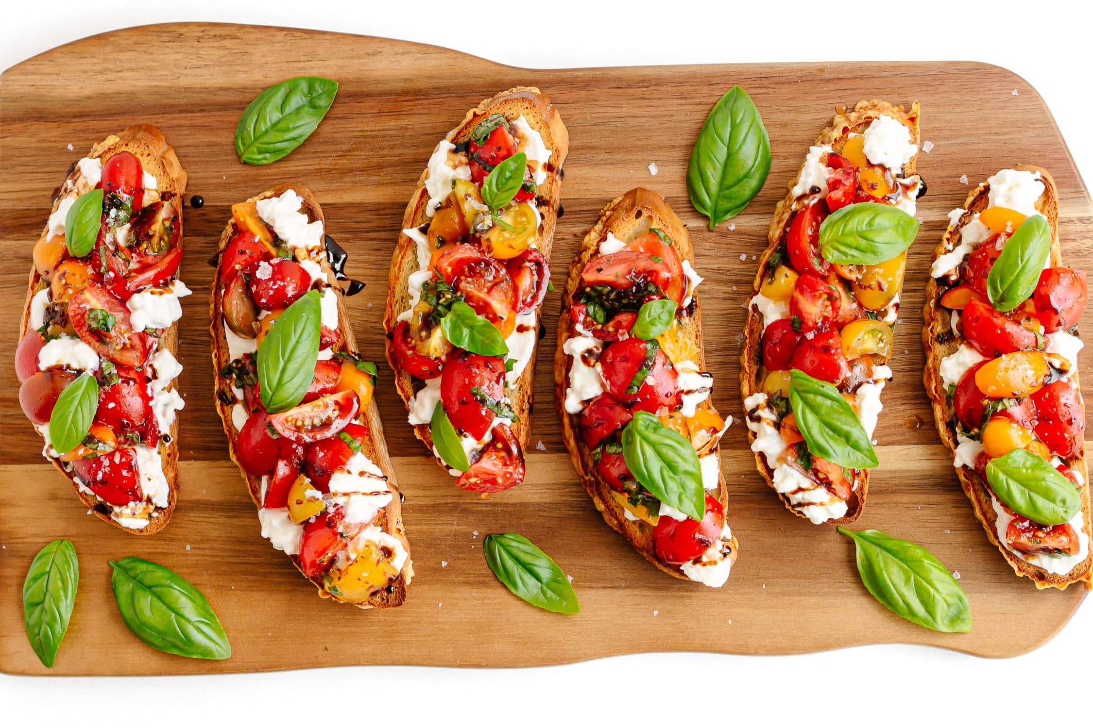 Burrata bruschetta with tomato and basil topping arranged on a wooden serving board.